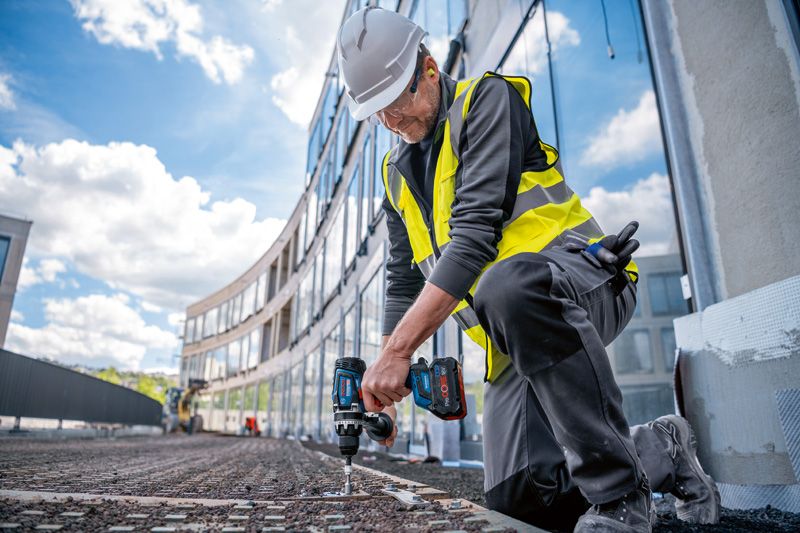 En person iført sikkerhedsudstyr bruger en batteridrevet boremaskine på en byggeplads.